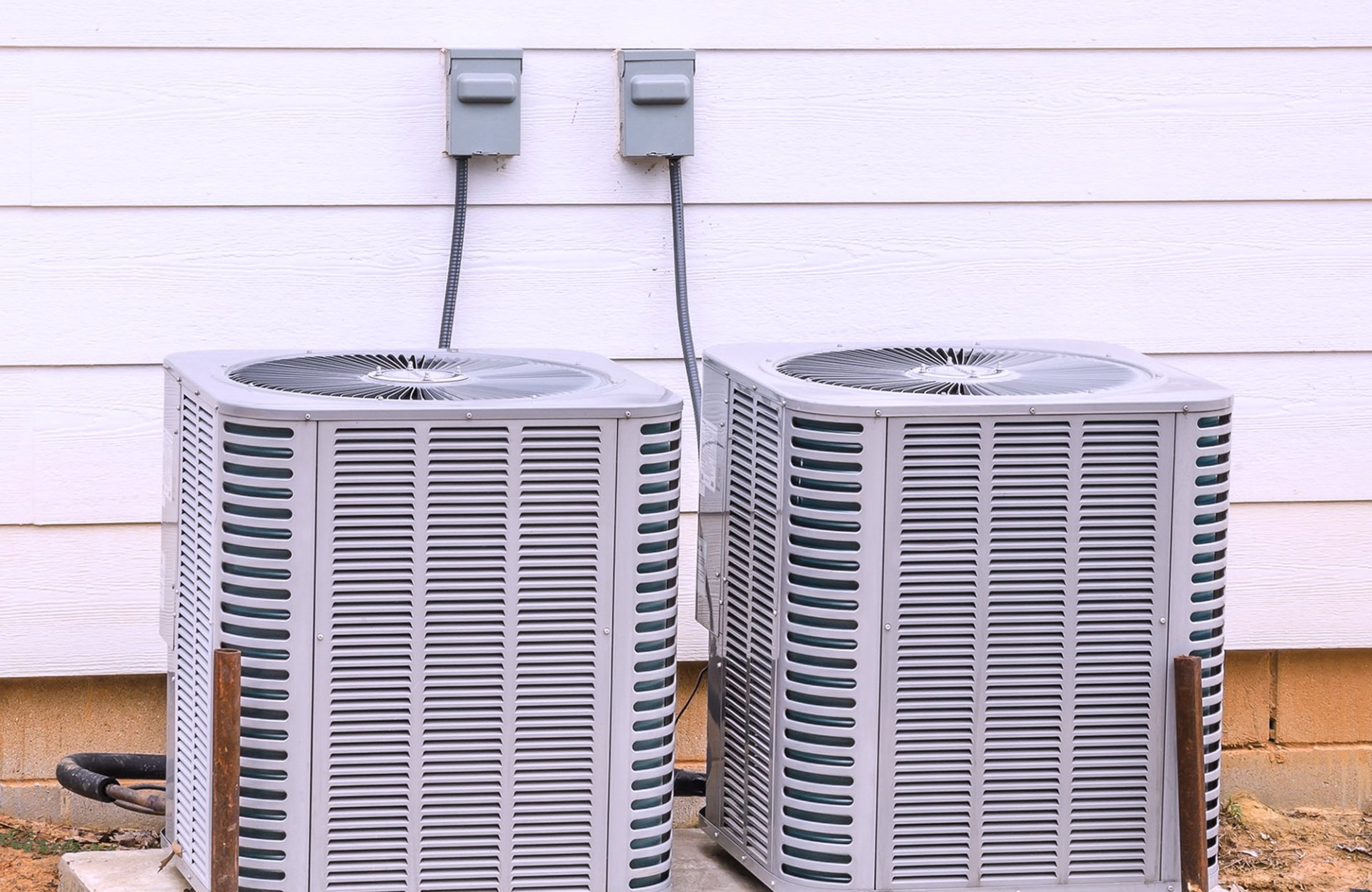 Two residential air conditioning condensers installed beside a home