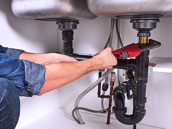 Plumber tightening a drain fitting under a kitchen sink